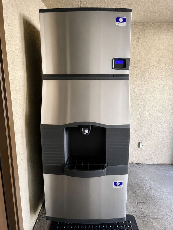 A stainless steel refrigerator with a water dispenser, located in a room with a textured wall and a concrete floor. - Burbank Inn and Suites (Burbank)