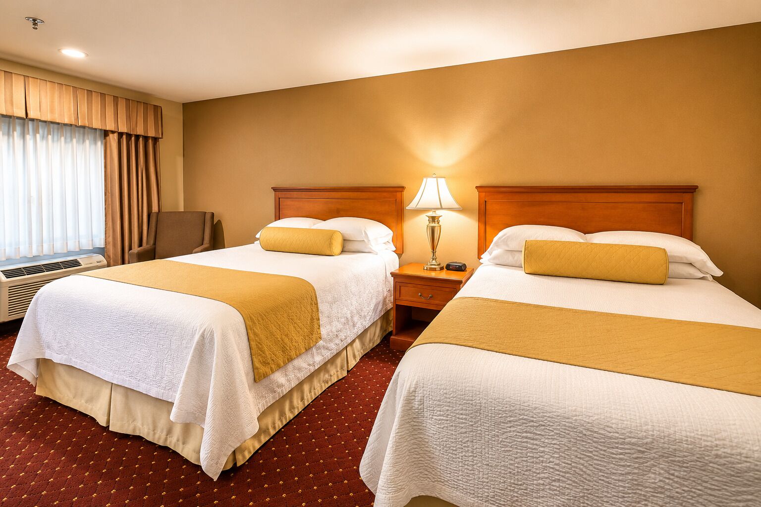 A hotel room with two beds, a nightstand with a lamp, a chair, and a window with curtains.