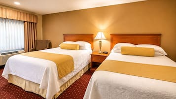 A hotel room with two beds, a nightstand with a lamp, a chair, and a window with curtains.