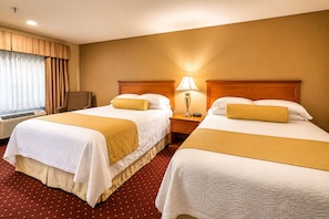 A hotel room with two beds, a nightstand with a lamp, a chair, and a window with curtains.