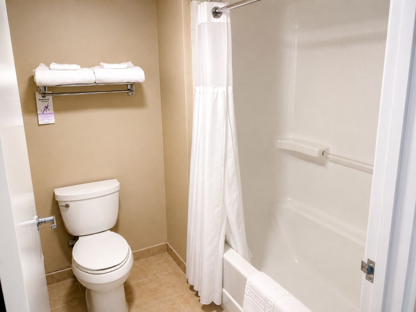 A bathroom with a toilet, a shower with a glass door, and a towel rack with folded towels.