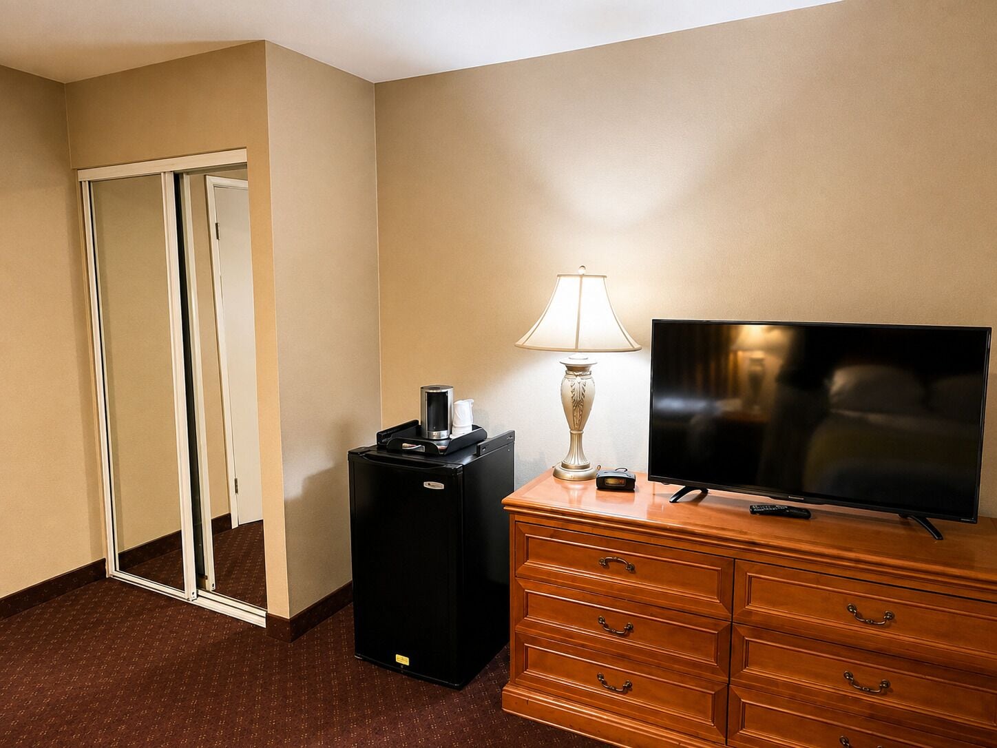 A hotel room with a flat-screen TV, a lamp, a coffee maker, and a dresser.