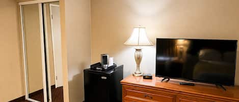 A hotel room with a flat-screen TV, a lamp, a coffee maker, and a dresser.