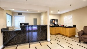 A hotel lobby with a reception desk, a kitchenette, and a seating area.
