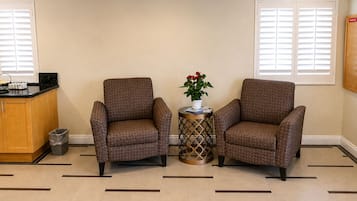 Una habitación con dos sillones, una mesita con un florero y una cocina, además de un cubo de basura.
