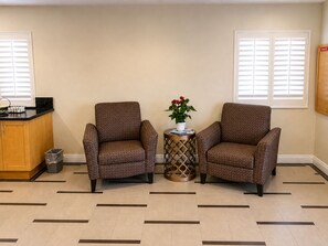 Una habitación con dos sillones, una mesita con un florero y una cocina, además de un cubo de basura.