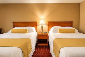 Una habitación de hotel con dos camas, una mesita de noche con lámpara y una alfombra roja con lunares.