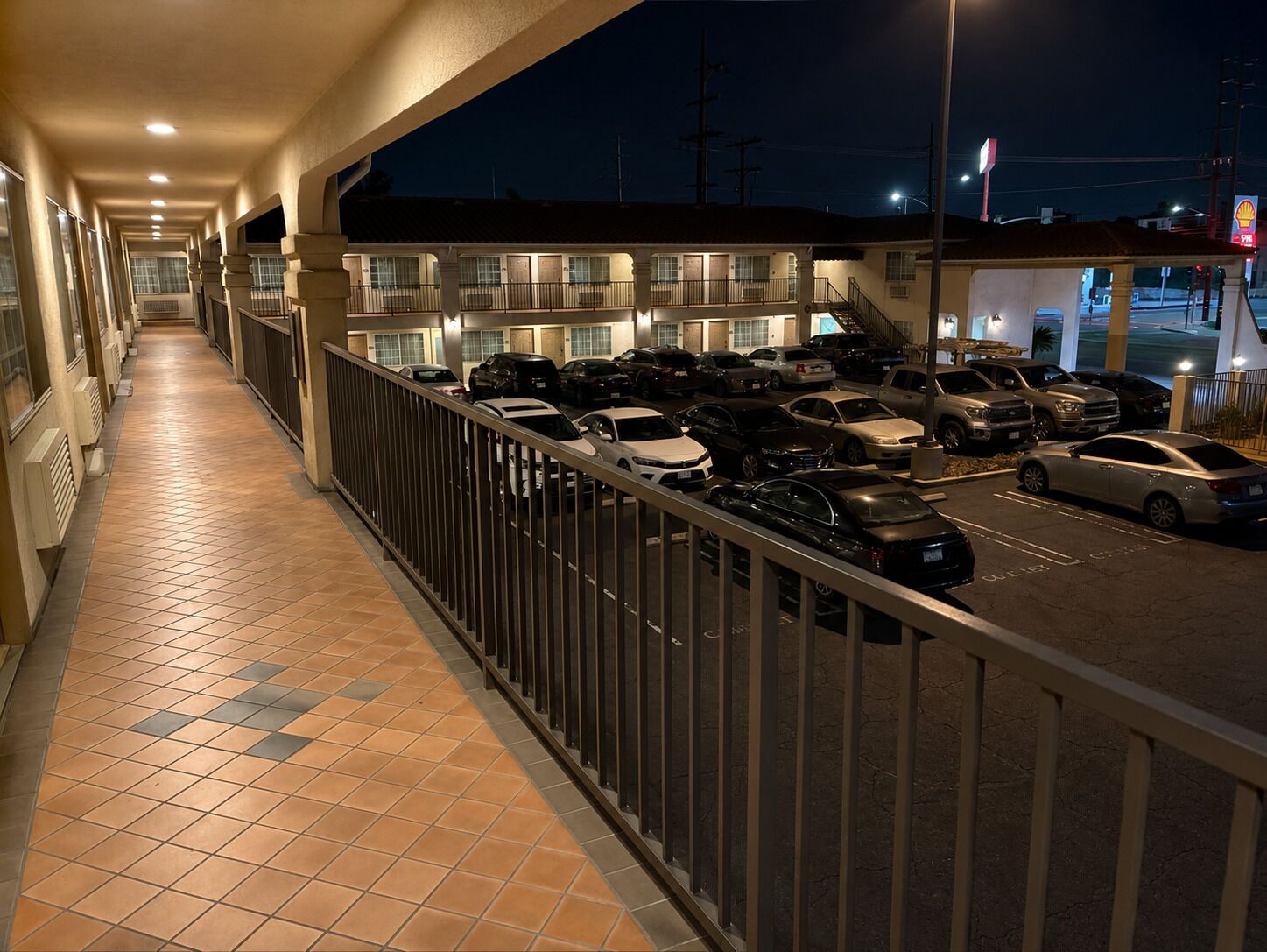 A hotel corridor with a tiled floor, a railing, and a parking lot with cars.