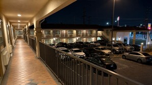 A hotel corridor with a tiled floor, a railing, and a parking lot with cars.