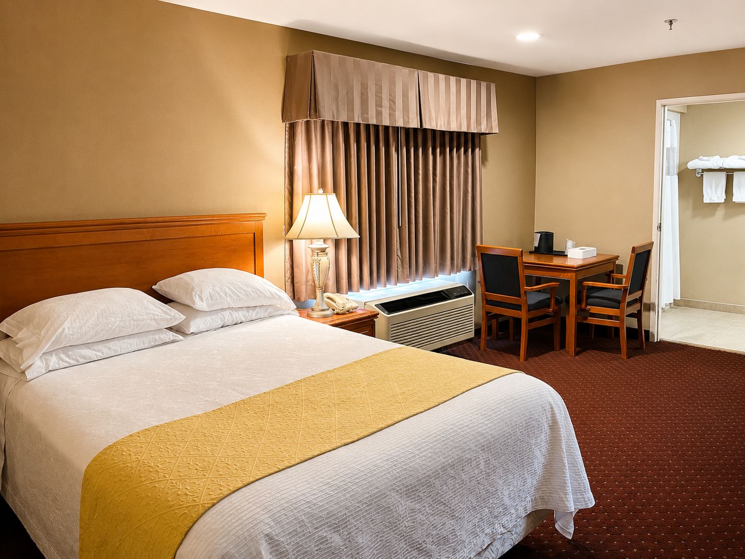 A hotel room with a bed, a desk, a chair, a lamp, and a window with curtains.