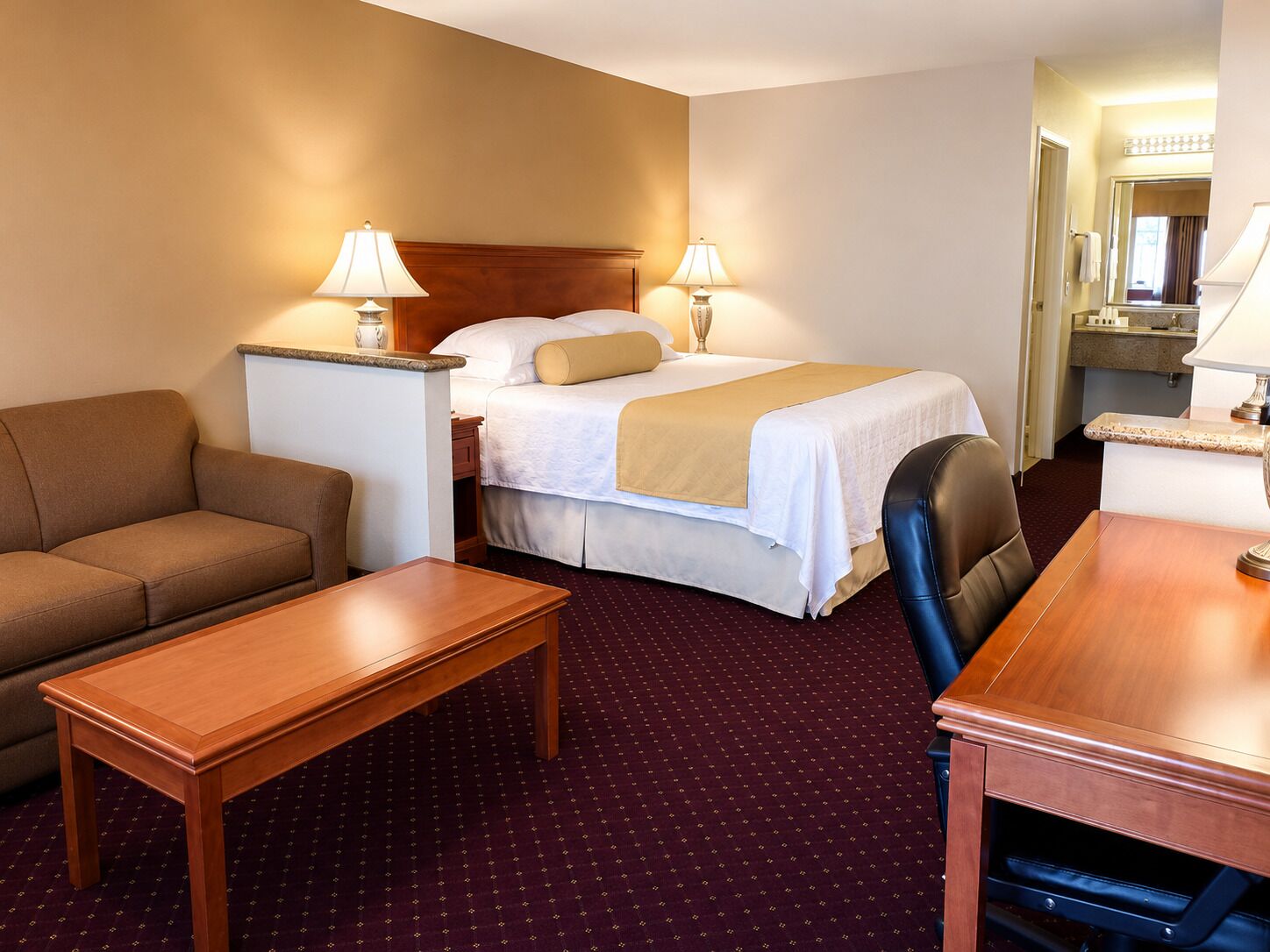 A hotel room with a bed, a sofa, a desk, and a bathroom visible in the background.