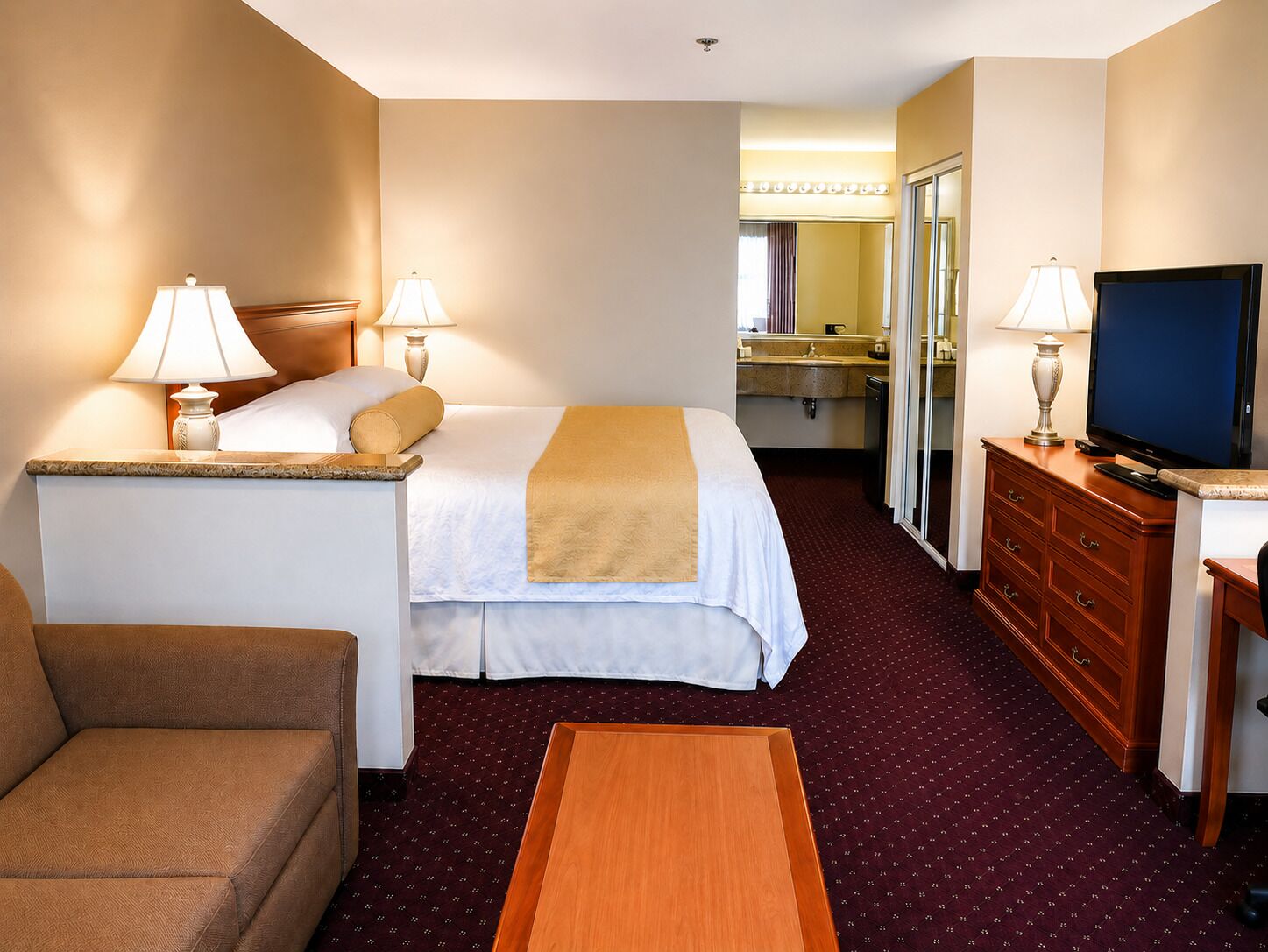 Habitación de hotel con cama, lámparas de noche, televisor, cómoda, escritorio y una silla.