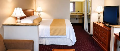 Habitación de hotel con cama, lámparas de noche, televisor, cómoda, escritorio y una silla.