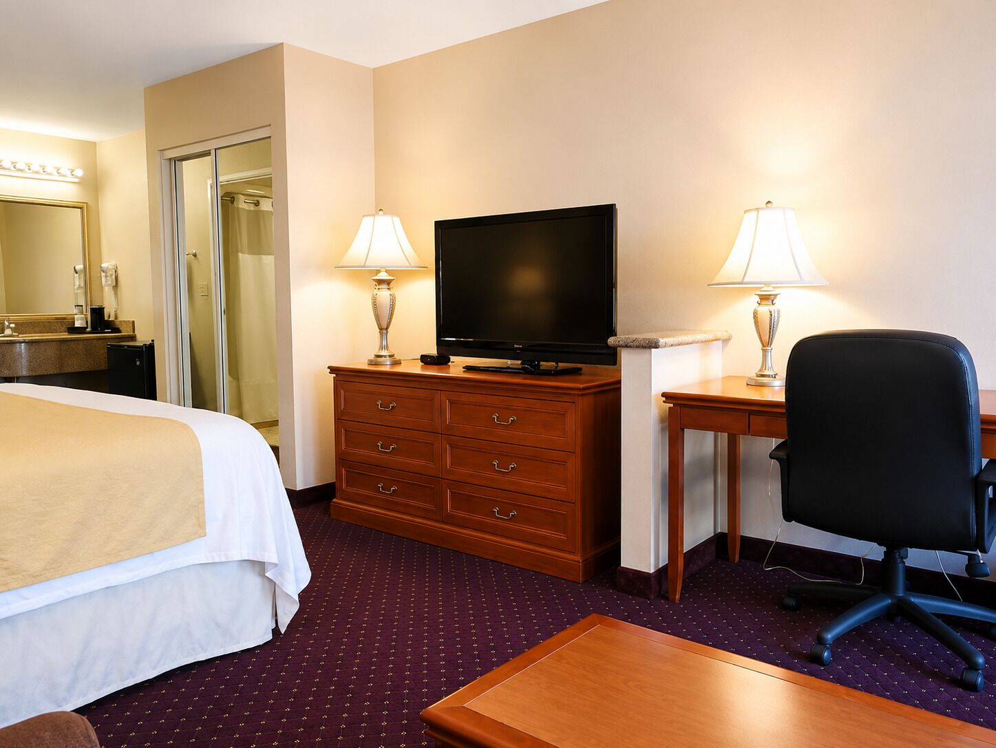 A hotel room with a bed, a desk with a chair, a television, and a dresser.