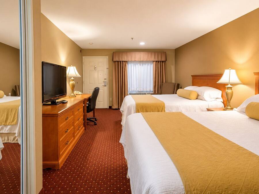 A hotel room with two beds, a desk with a television, and a chair.