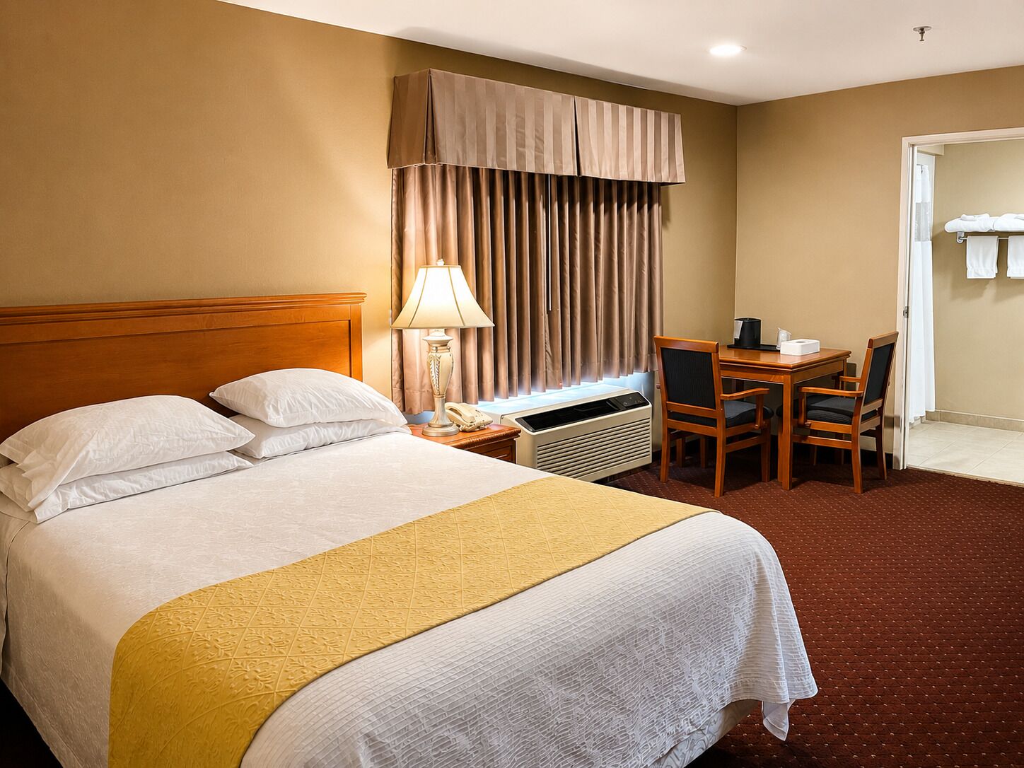 Une chambre d’hôtel avec un lit, un bureau, une chaise, une lampe et une fenêtre avec des rideaux.