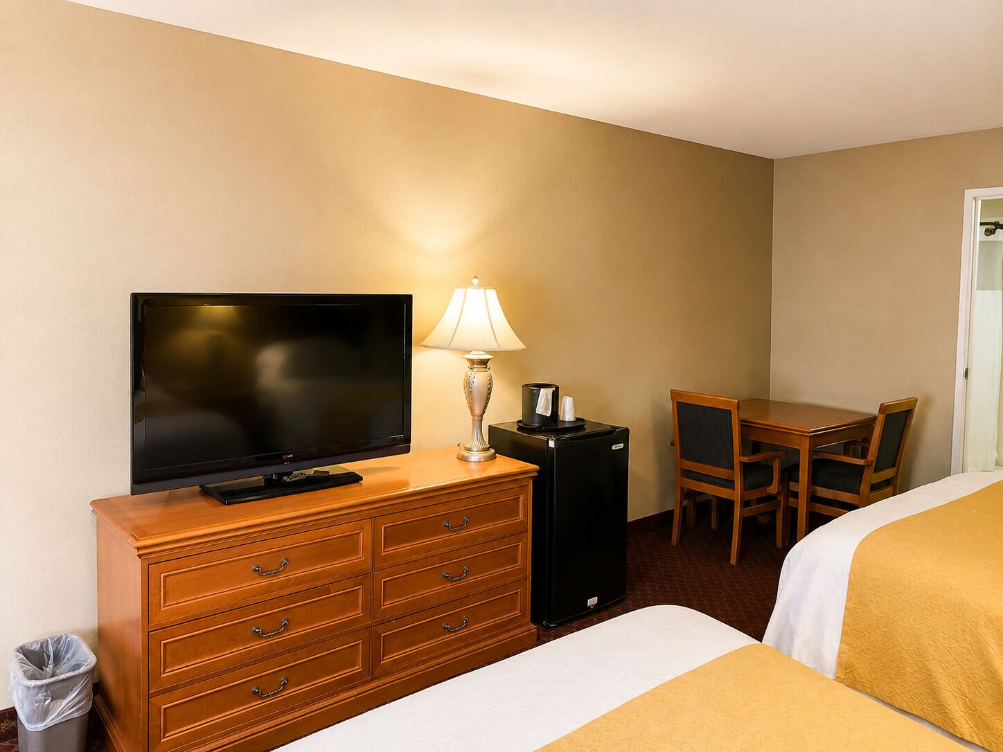Una habitación de hotel con televisión, escritorio, silla, lámpara y cesto de basura.
