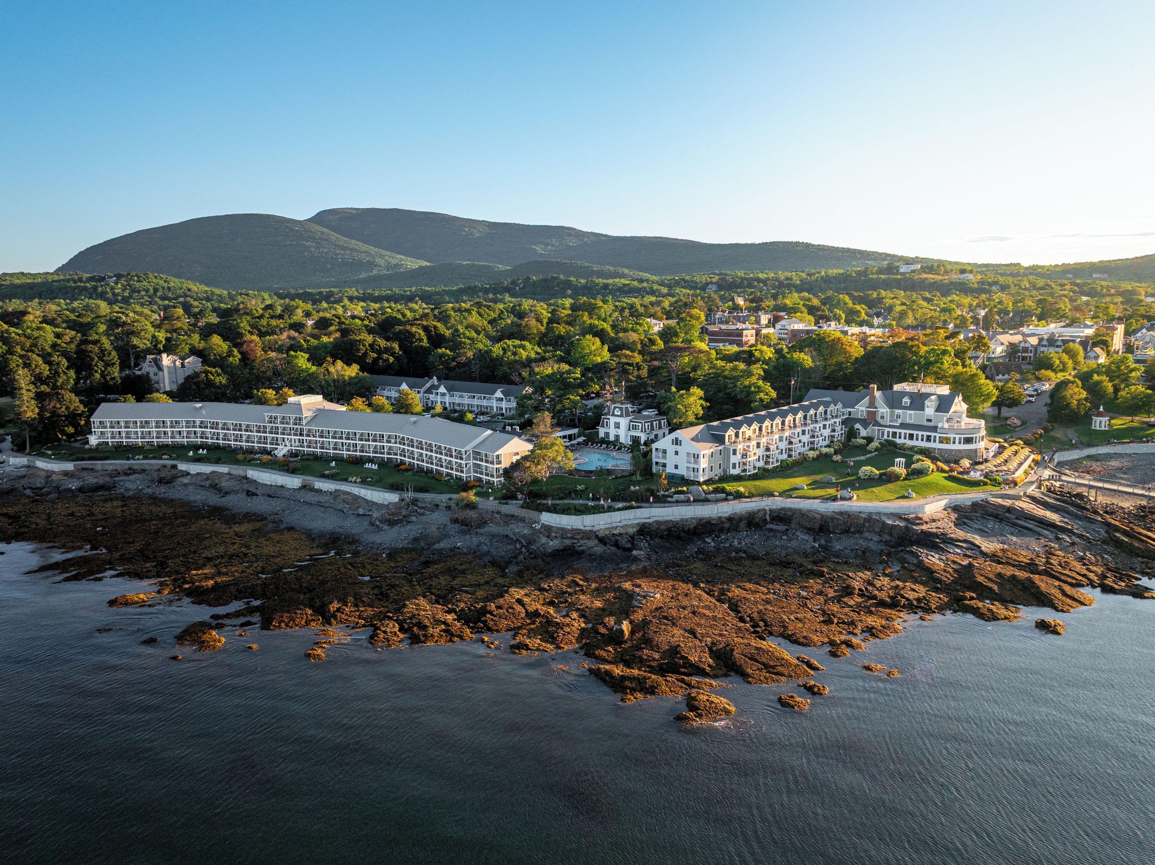 A coastal resort with multiple buildings, a swimming pool, and a rocky shoreline.