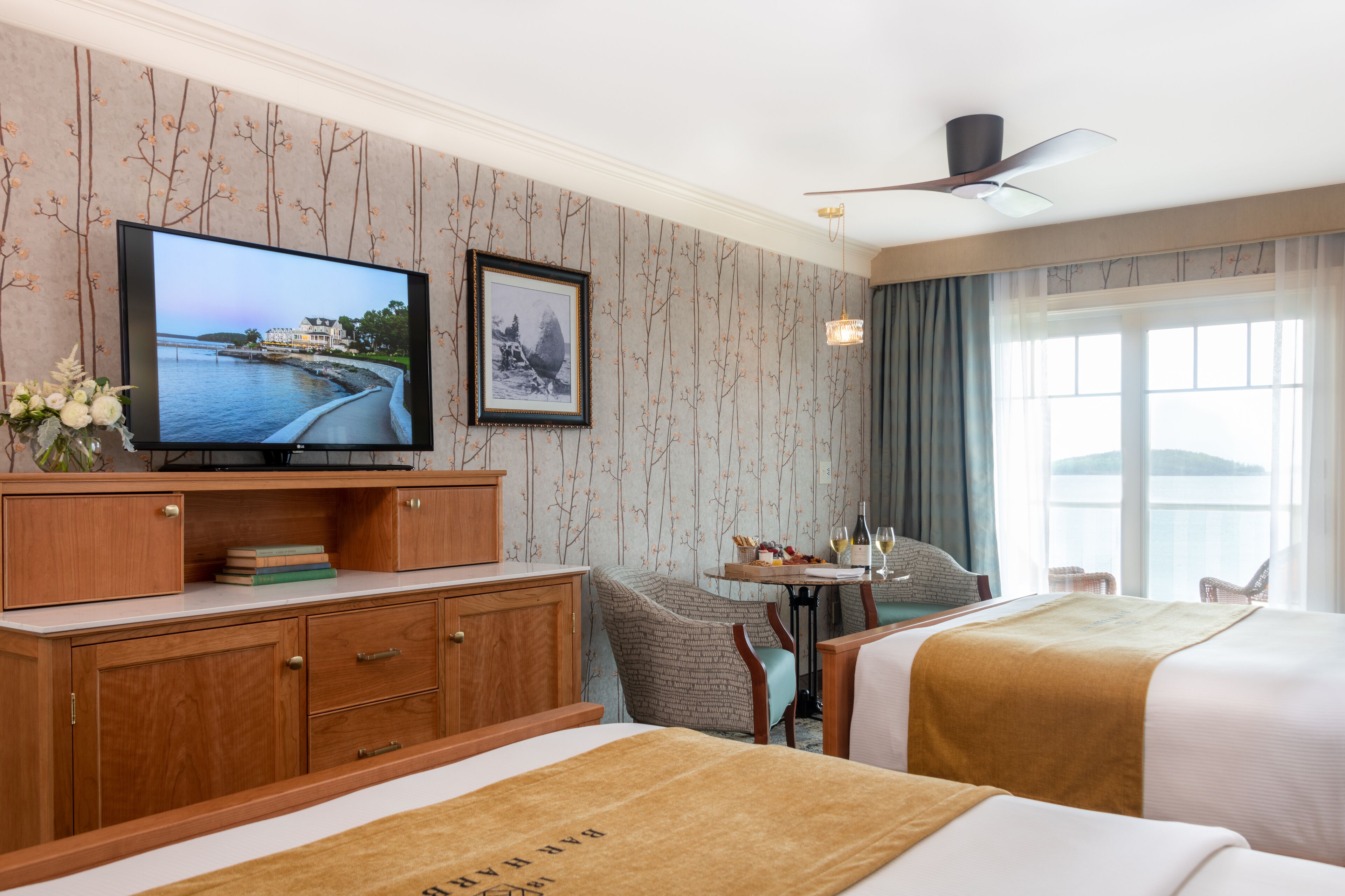 Habitación de hotel con televisión, un cuadro enmarcado, escritorio con lámpara, una silla y cama con cabecera.