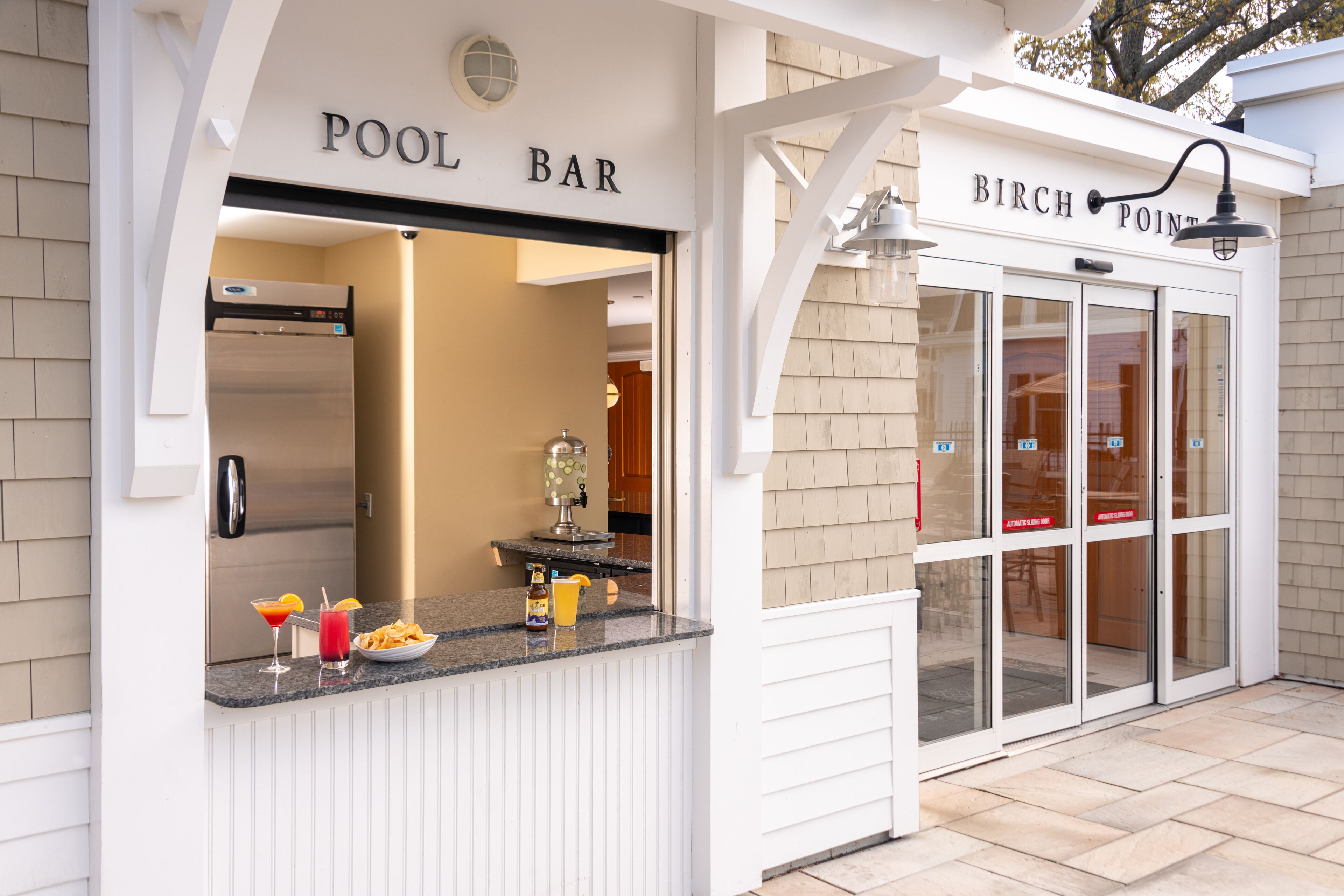 A pool bar with a counter displaying drinks and a refrigerator.