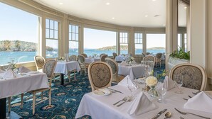 Un comedor con mesas dispuestas para el servicio, amplios ventanales con vistas al mar y suelo cubierto de alfombra.