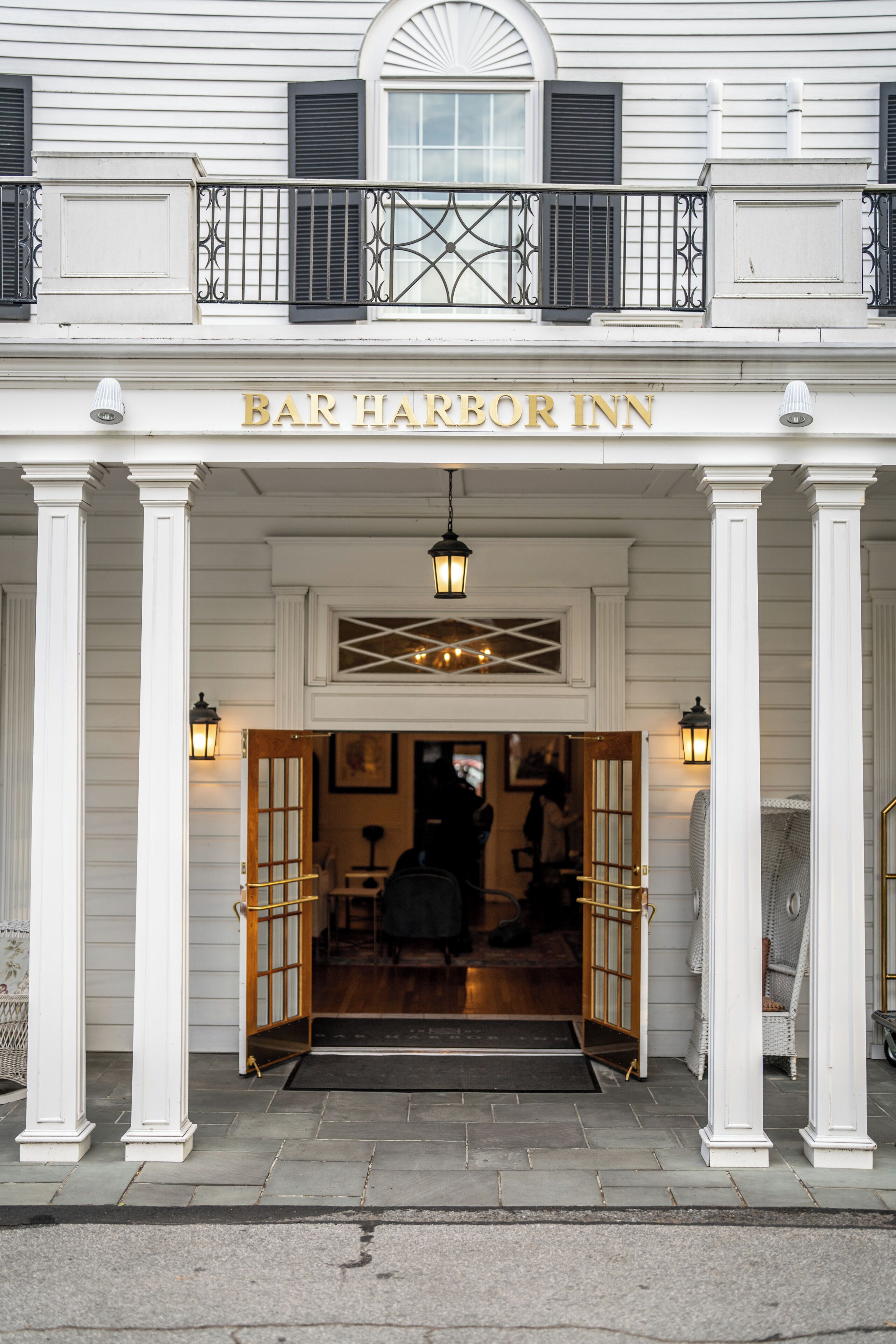 The entrance to Bar Harbor Inn with a double door, a balcony with black shutters, and a sign above the doors.