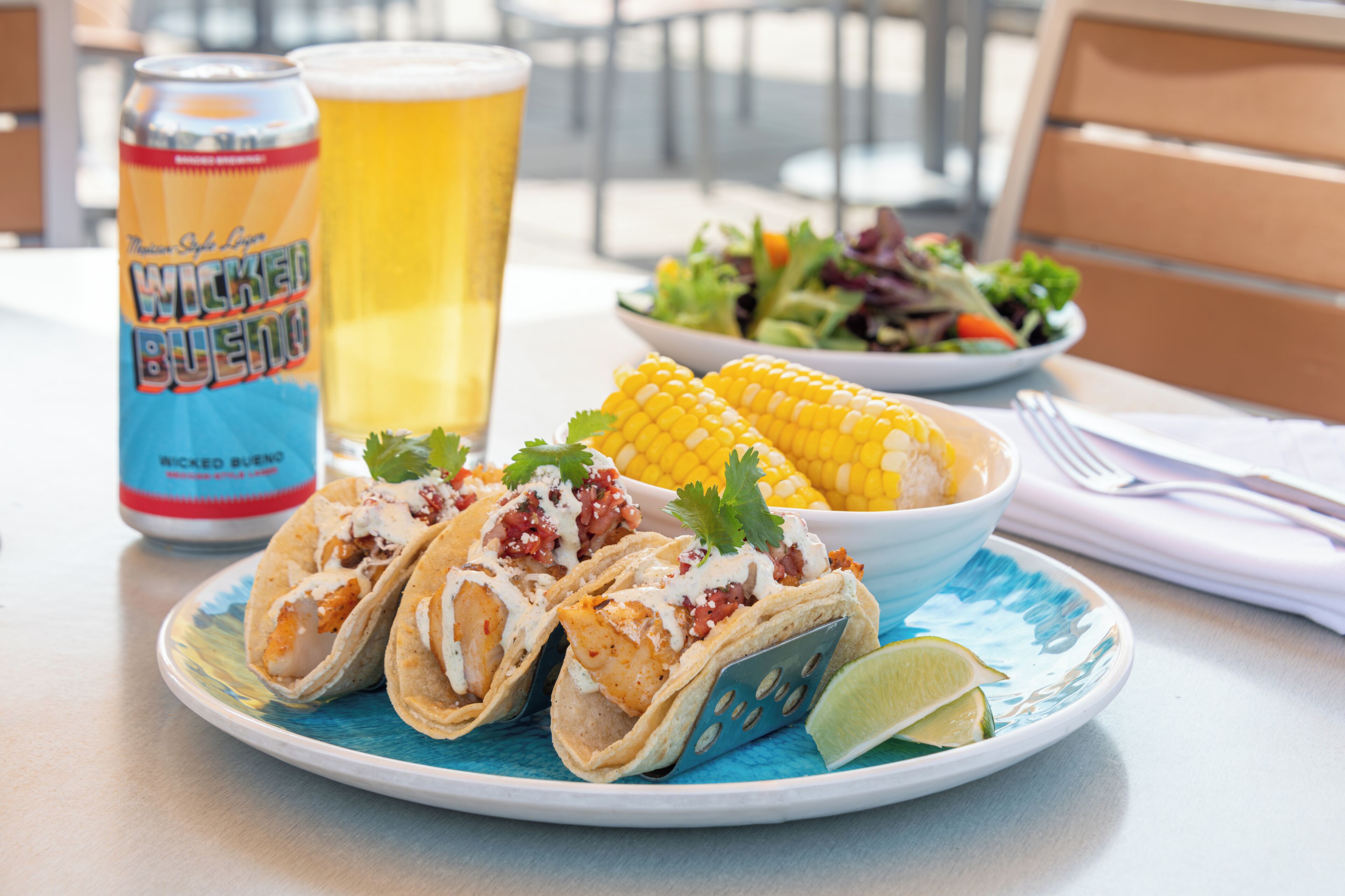 Un plato de tacos, una lata de cerveza, un vaso de cerveza y una ensalada acompañante sobre una mesa.