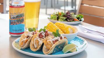 Un plato de tacos, una lata de cerveza, un vaso de cerveza y una ensalada acompañante sobre una mesa.