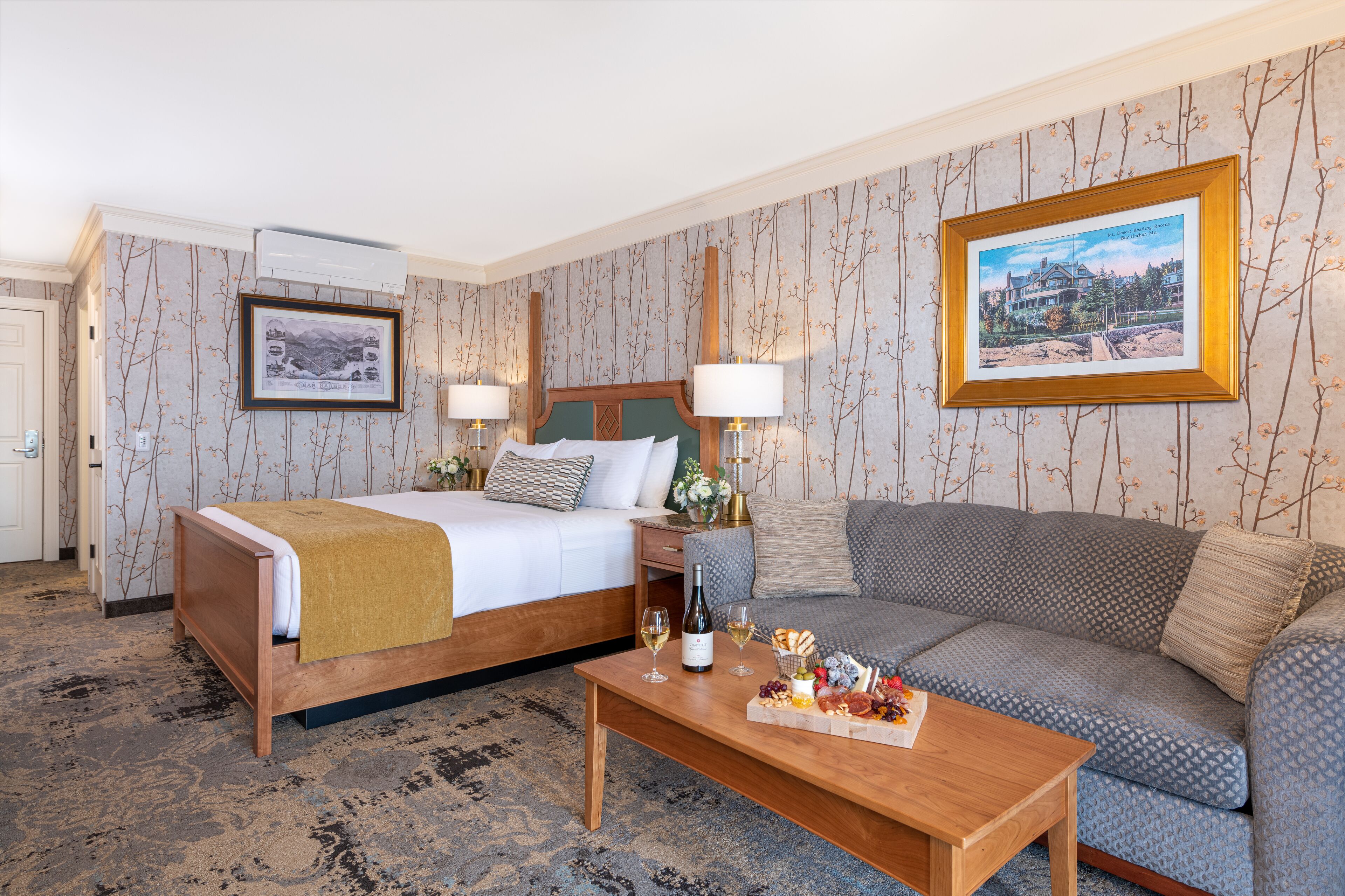 A hotel room with a bed, a sofa, a coffee table with snacks and wine, and two wall-mounted lamps.