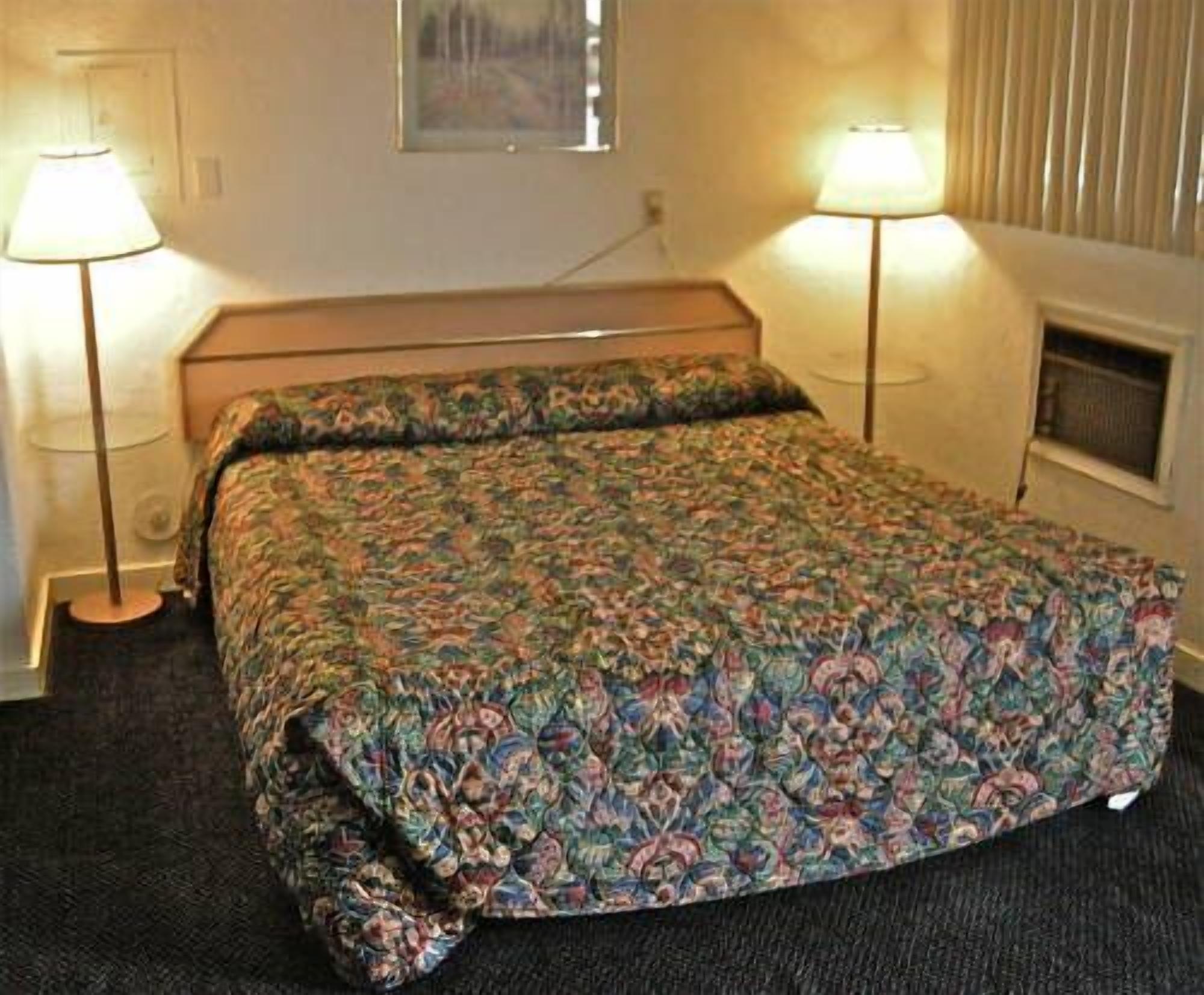 Een hotelkamer met een bed, twee bedlampjes, een raam met zonwering en een aan de muur hangend schilderij.