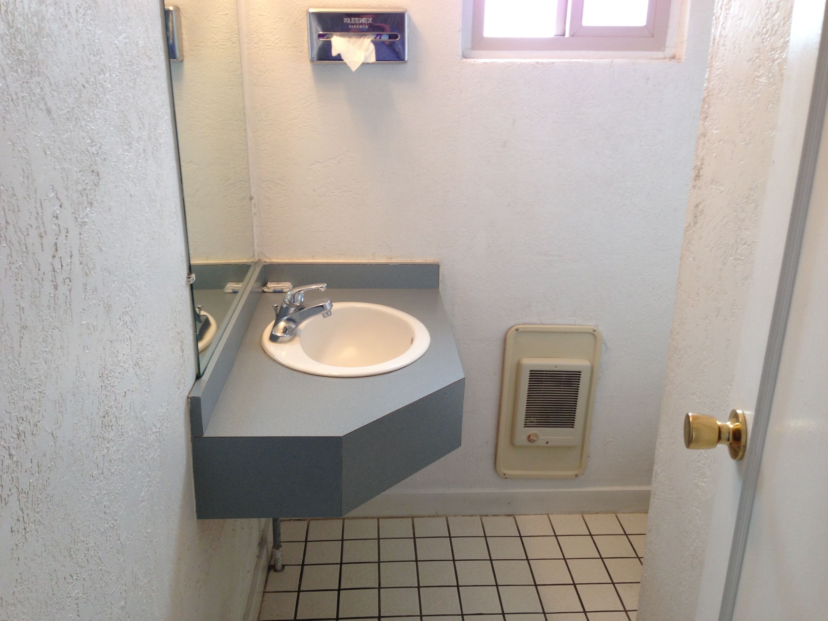 A small bathroom with a white sink, a mirror, and a window above the sink.