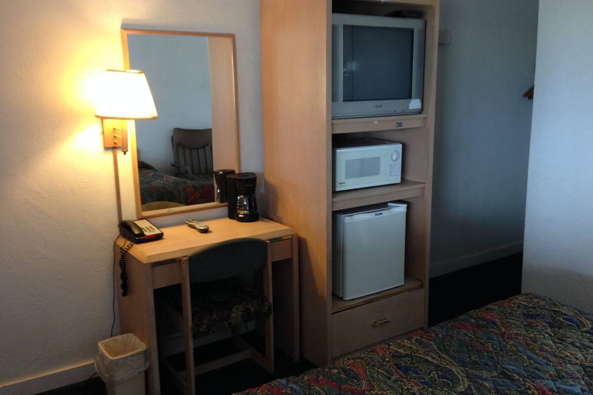 Une chambre d’hôtel équipée d’un bureau, d’un miroir, d’une télévision, d’un four à micro-ondes, d’un réfrigérateur, d’un lit et d’une table de chevet.
