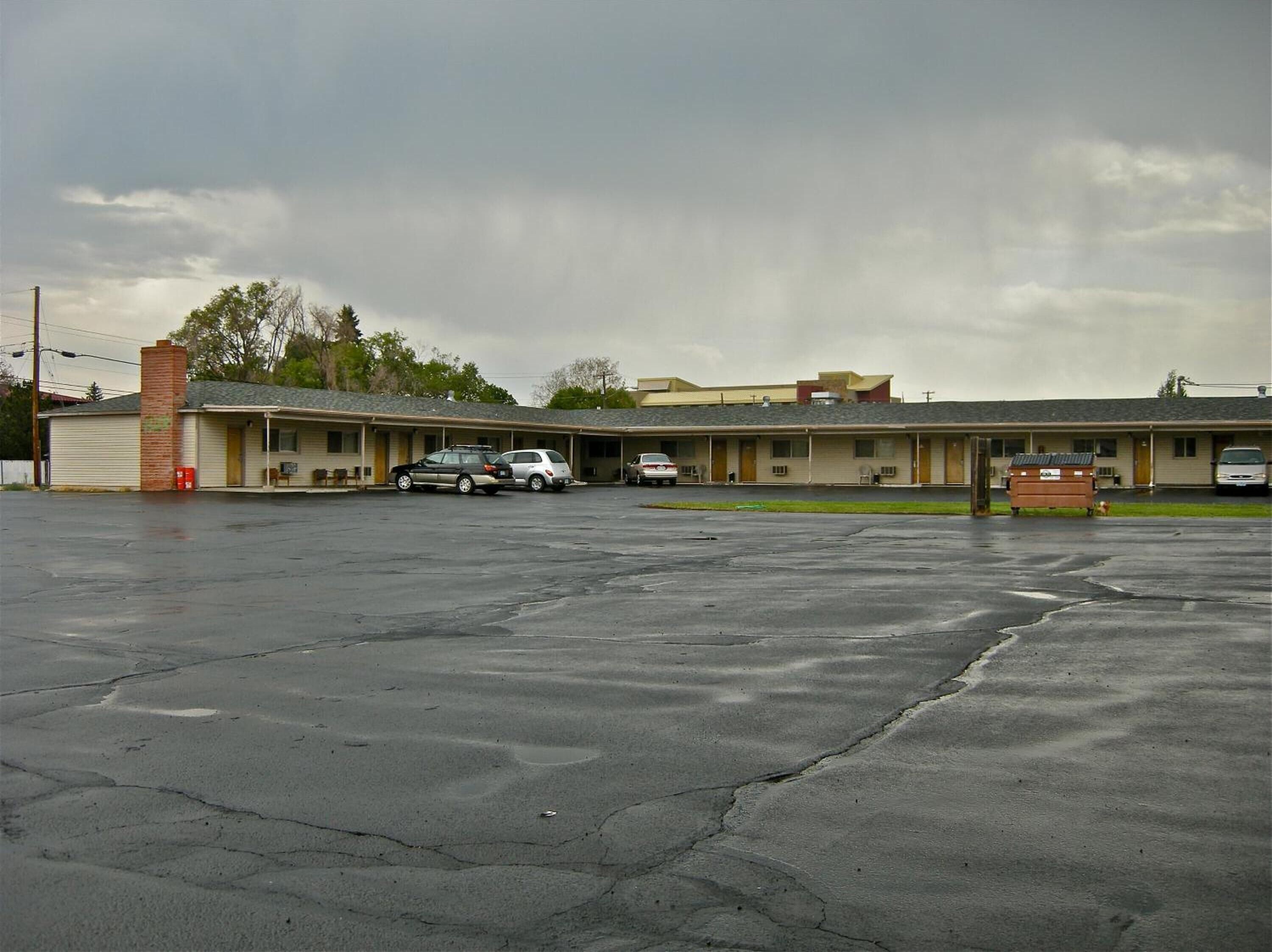 A motel with a parking lot, a brick chimney, and a row of rooms.
