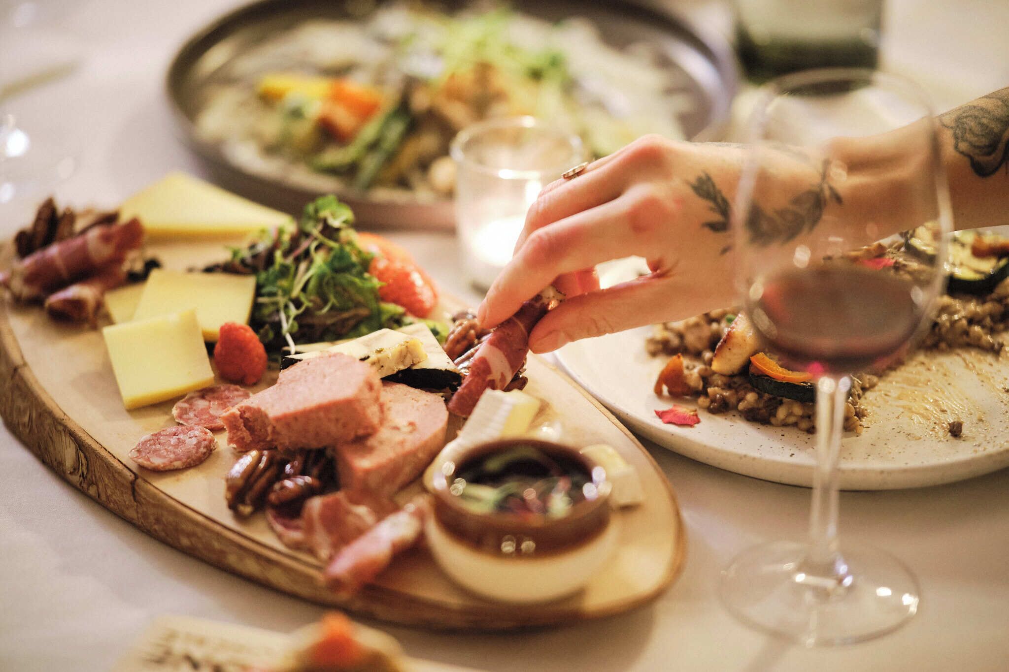 Una tabla de embutidos con diferentes carnes, quesos y frutos secos, acompañada de una copa de vino tinto.
