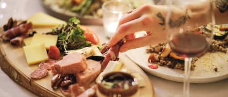 Una tabla de embutidos con diferentes carnes, quesos y frutos secos, acompañada de una copa de vino tinto.
