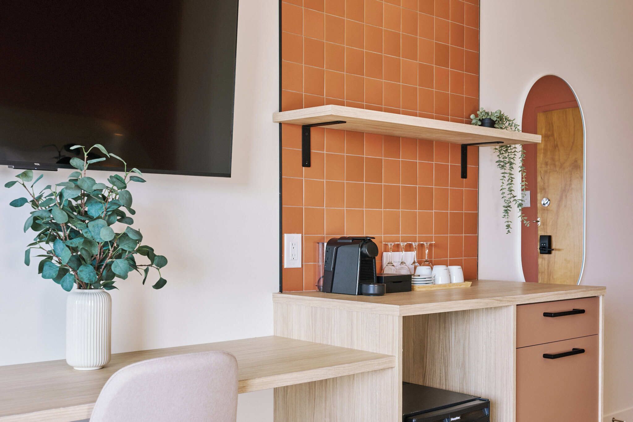 Una kitchenette con cafetera, una planta y un televisor montado en la pared.