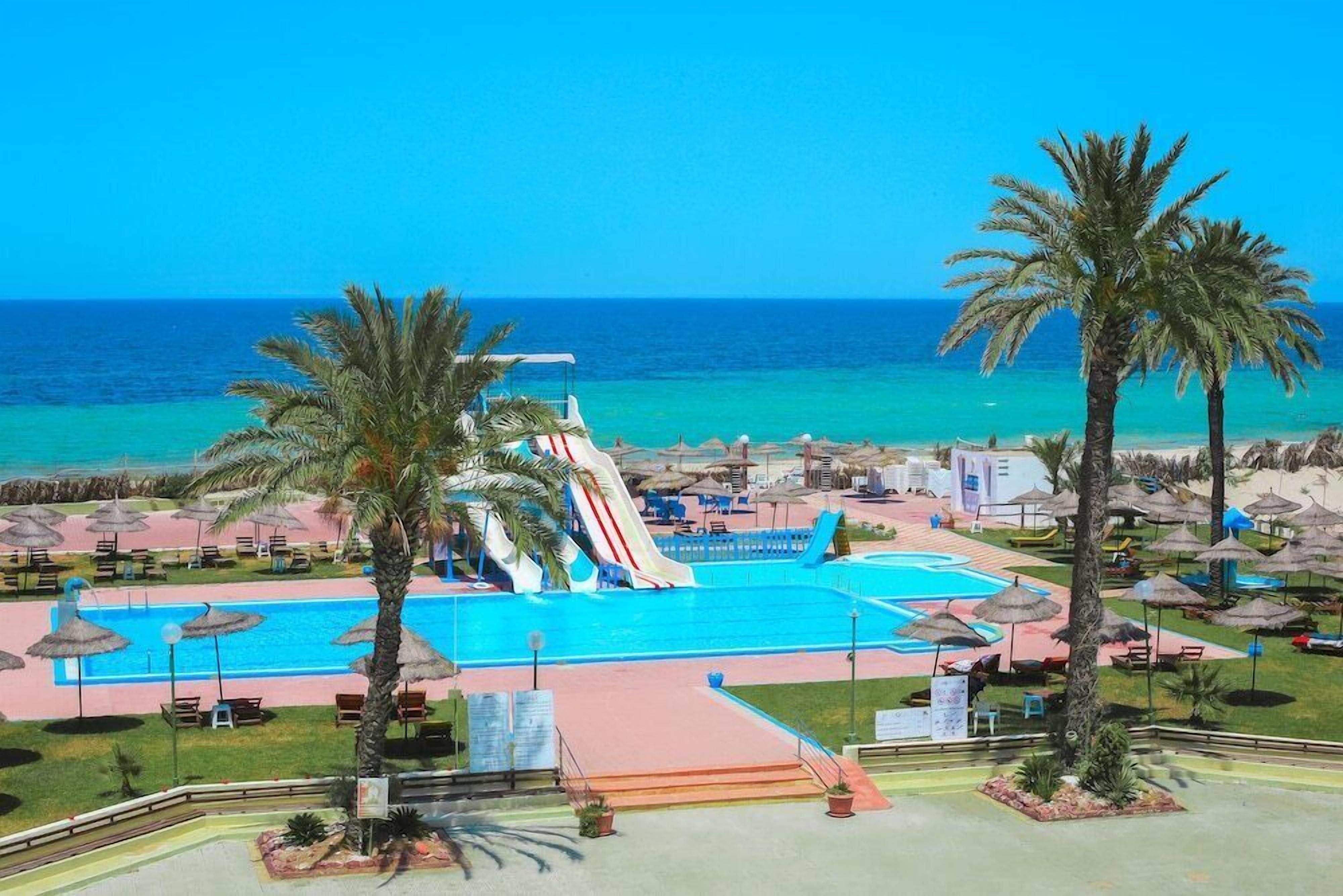 A resort with a swimming pool, palm trees, and a water slide.
