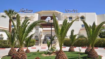 A hotel with a white facade, palm trees in the foreground, and signage in English and Arabic.