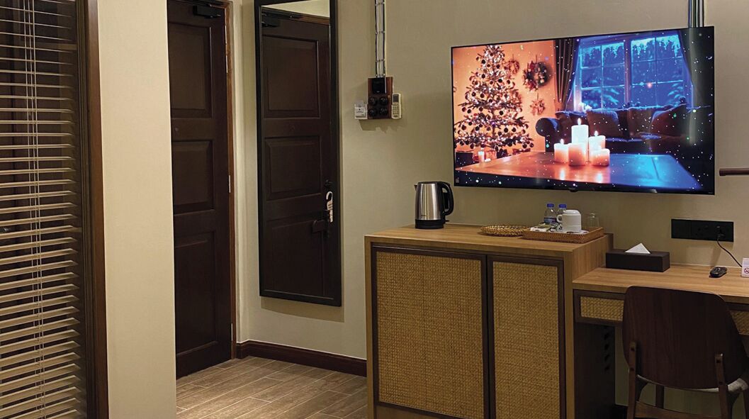 A hotel room with a TV mounted on the wall, a wooden desk, a chair, a cabinet, and a door.