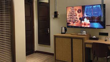 A hotel room with a TV mounted on the wall, a wooden desk, a chair, a cabinet, and a door.