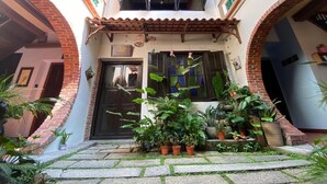 Un patio con una entrada central, plantas en macetas y techo de tejas.