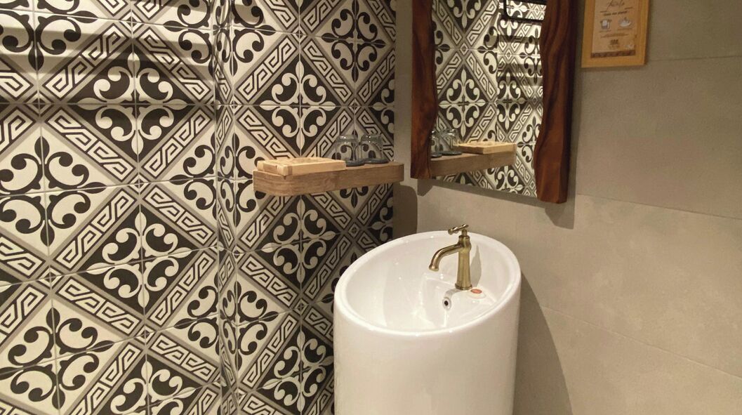 A bathroom with patterned tiles, a white sink, and wooden shelves.