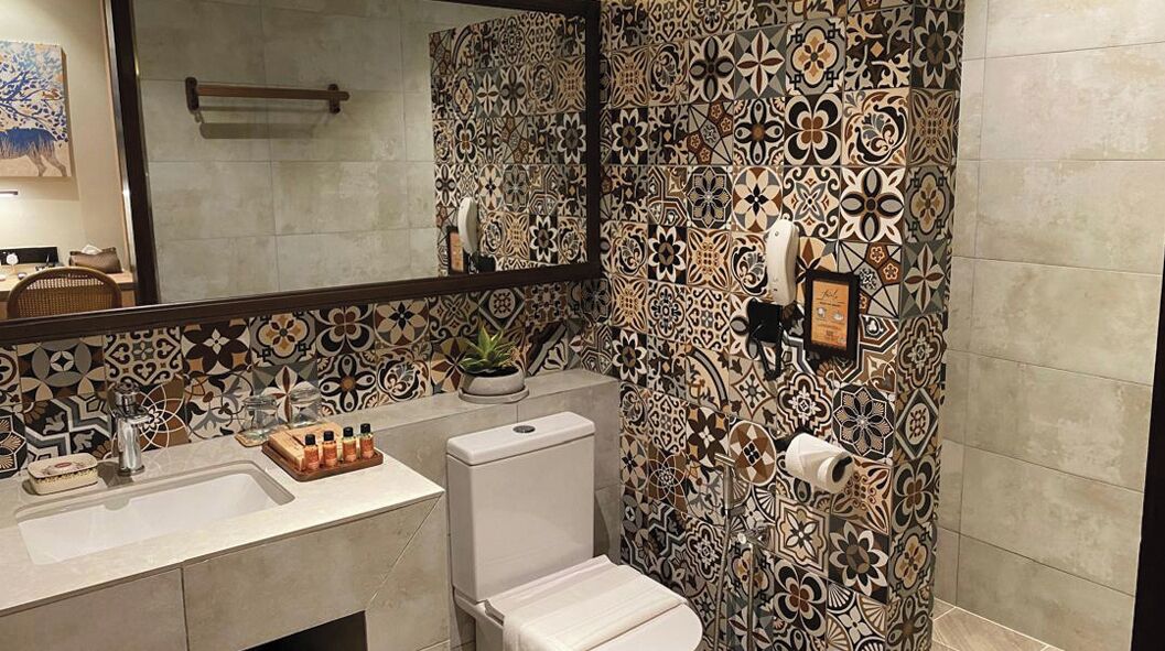 A bathroom with patterned tiles, a sink, a toilet, and a mirror.
