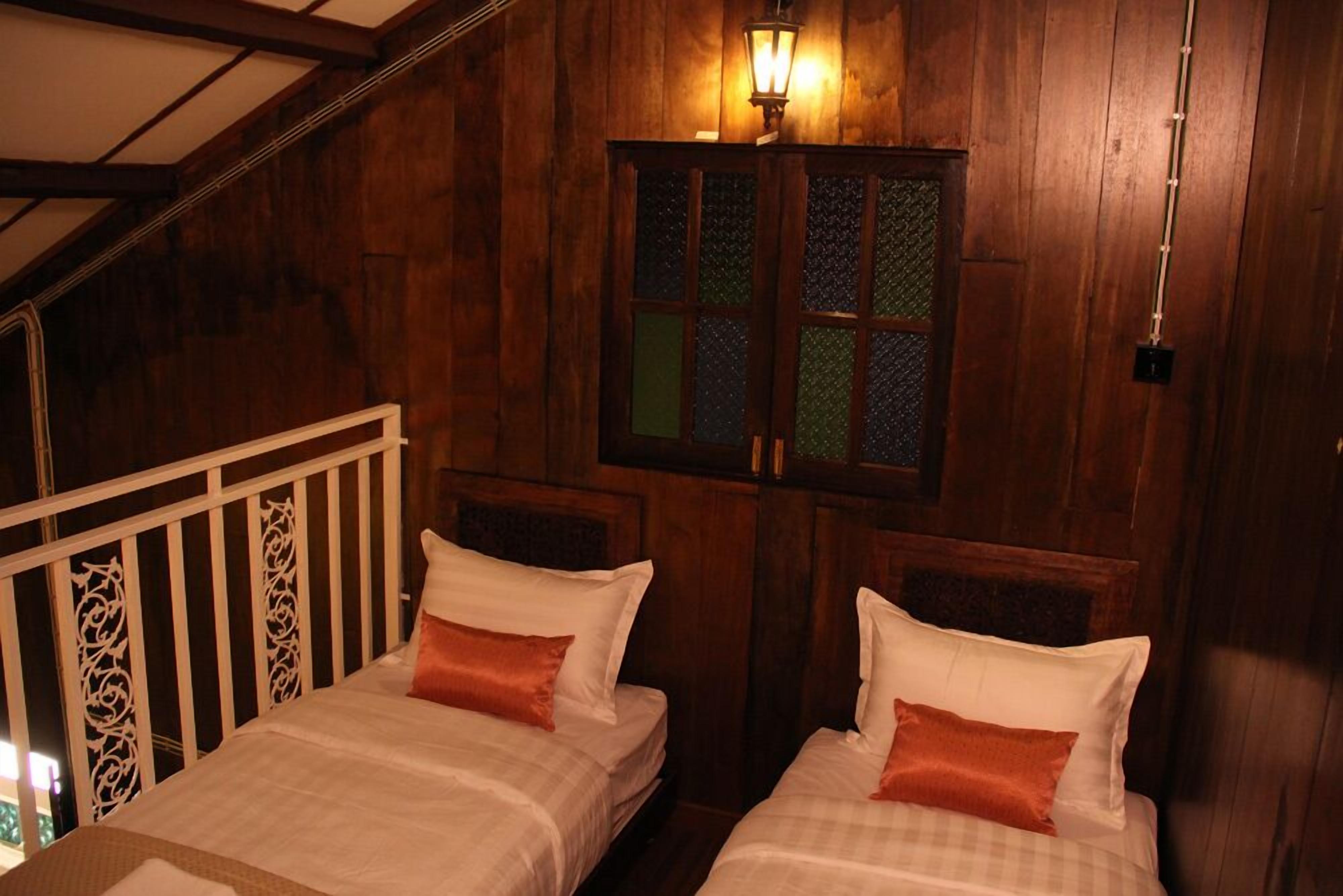 A wooden room with two beds, a window with a decorative screen, and a hanging light fixture.