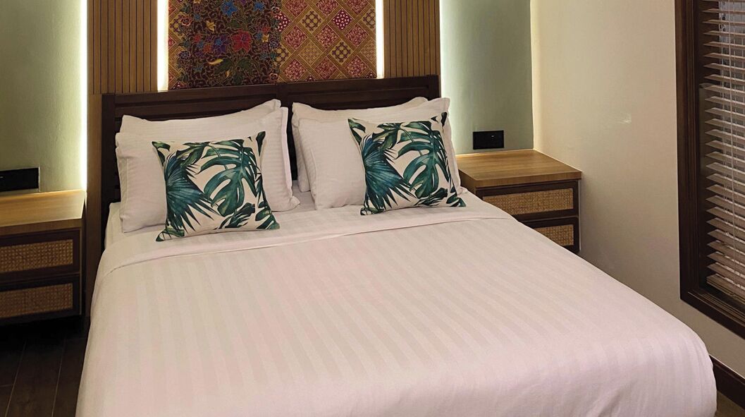 A neatly made bed with two pillows, a wooden headboard, and two bedside tables with woven baskets.
