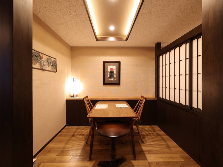 A dining area with a wooden table and chairs, a framed picture on the wall, and a traditional sliding door.