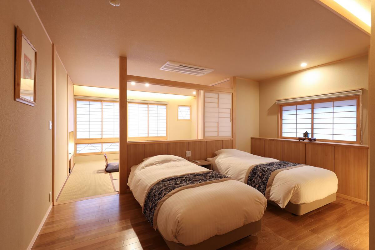 A room with two beds, wooden flooring, and large windows with traditional sliding doors.