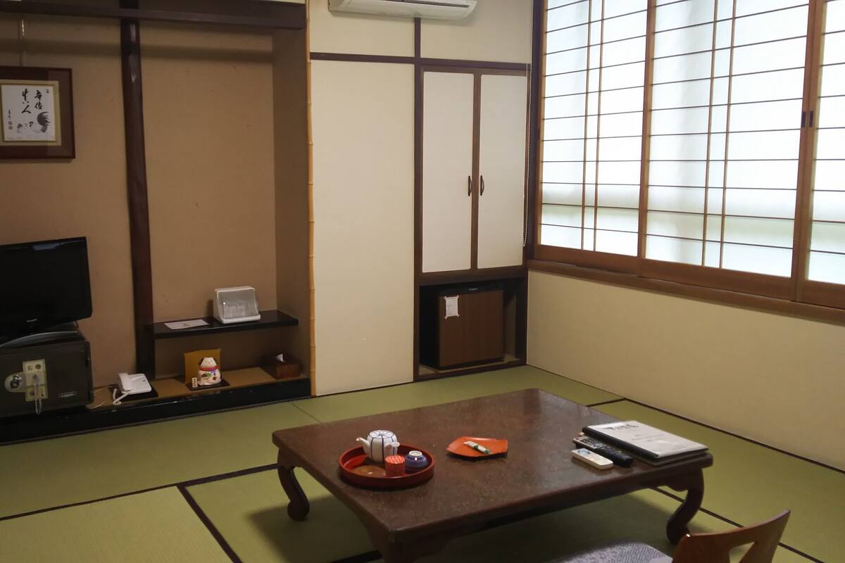 A traditional Japanese-style room with tatami flooring, a low table with tea set, a television, and sliding doors.