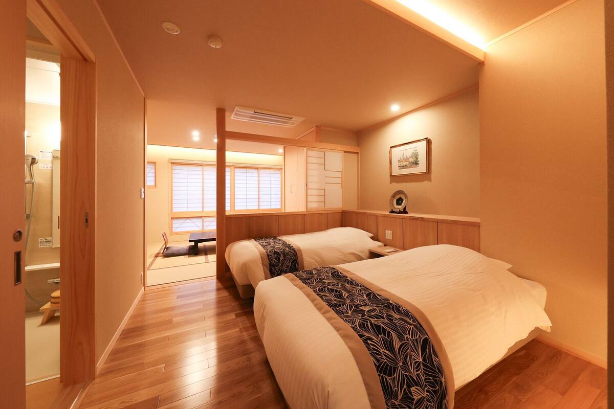 A hotel room with two beds, a wooden floor, a small table, and a picture on the wall.