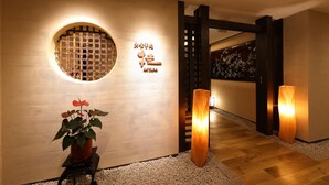 A modern interior with a wooden floor, a potted plant, and a wall-mounted light fixture. - Mutsumikan (Gero)